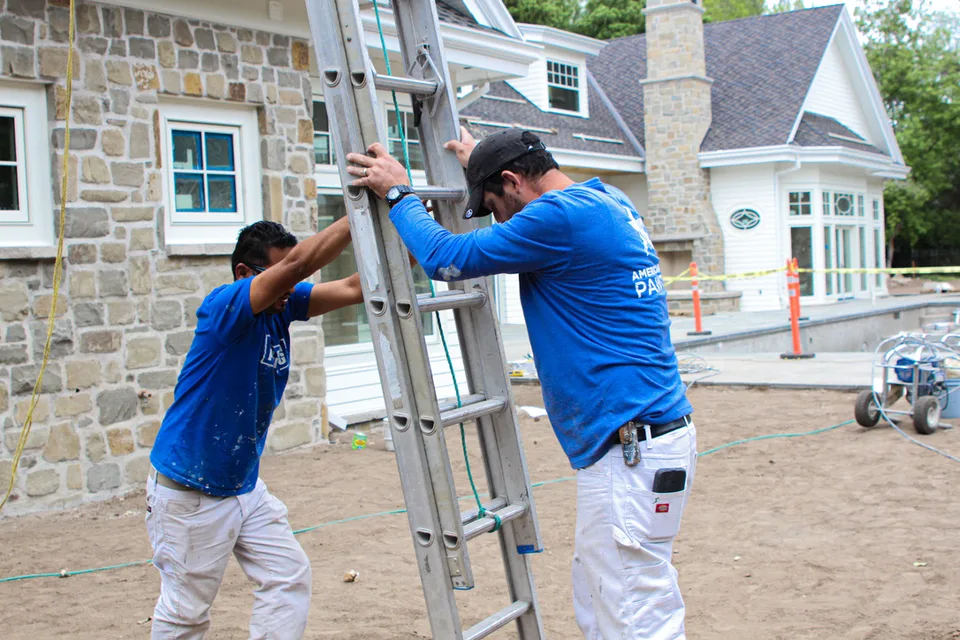 Two crew members on ladders at a stone house